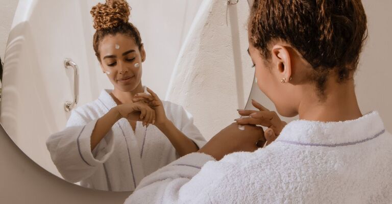 ragazza si applica la crema sul viso, davanti allo specchio
