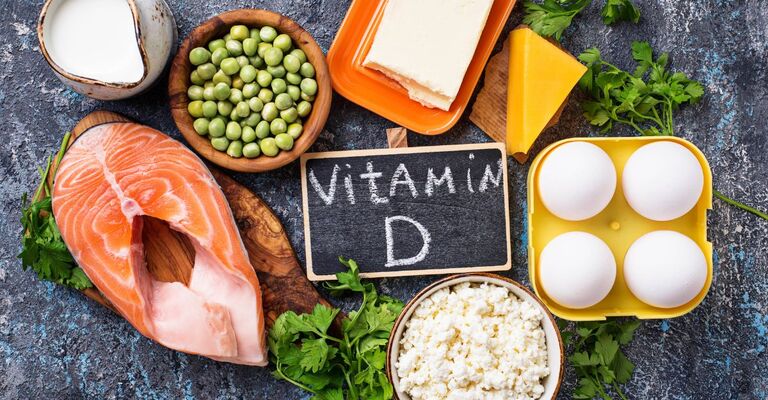 Composizione di alimenti ricchi di vitamina D, tra cui salmone, uova, formaggio e latte, con una piccola lavagna al centro.
