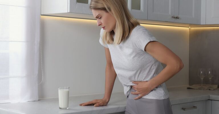 Una donna in cucina si tocca la pancia con un'espressione dolorante, guardando un bicchiere di latte sul bancone