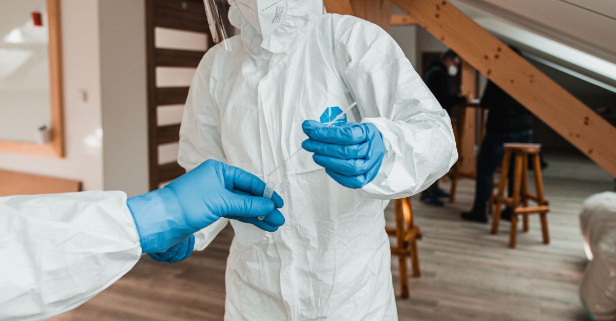 Operatore sanitario in tuta protettiva bianca e guanti azzurri mentre maneggia un tampone per test medico