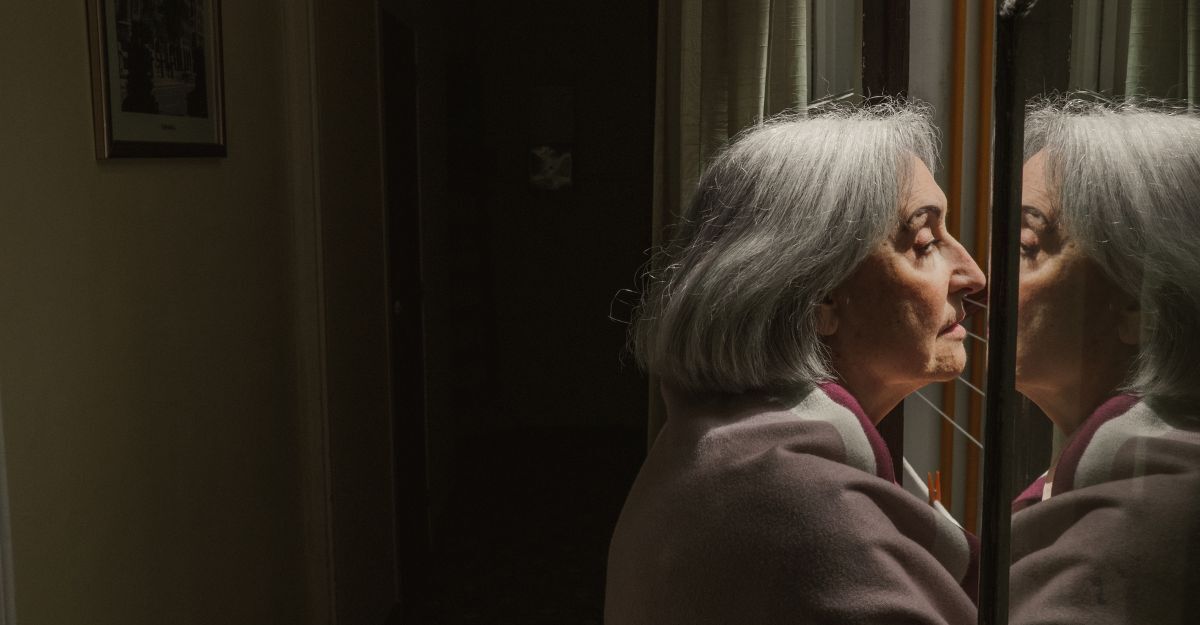 Una signora anziana, triste, guarda fuori dalla finestra