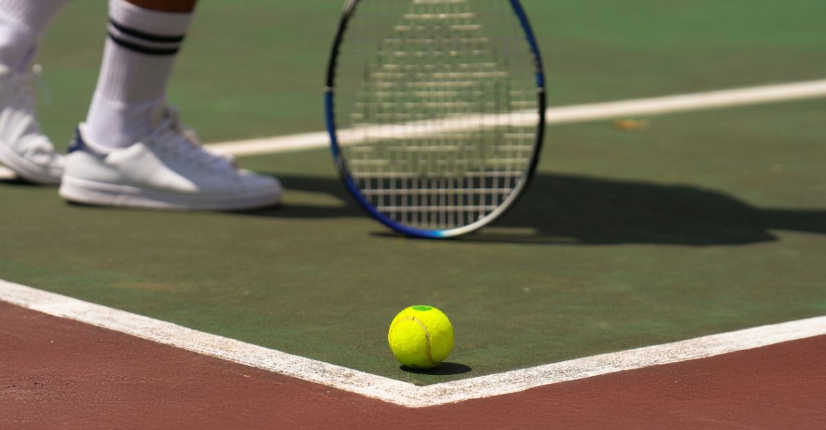 Il primo piano dei piedi di un giocatore di tennis, con racchetta in mano e pallina per terra