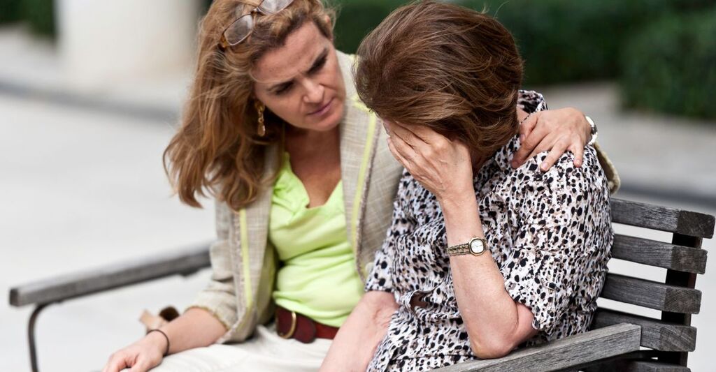 Una signora triste consolata dalla figlia su una panchina