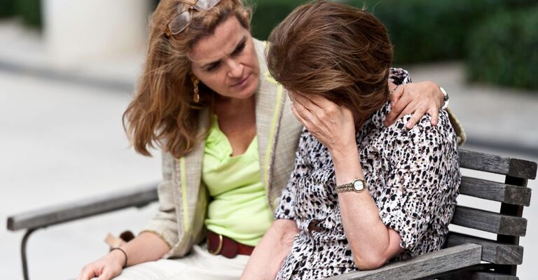 Una signora triste consolata dalla figlia su una panchina