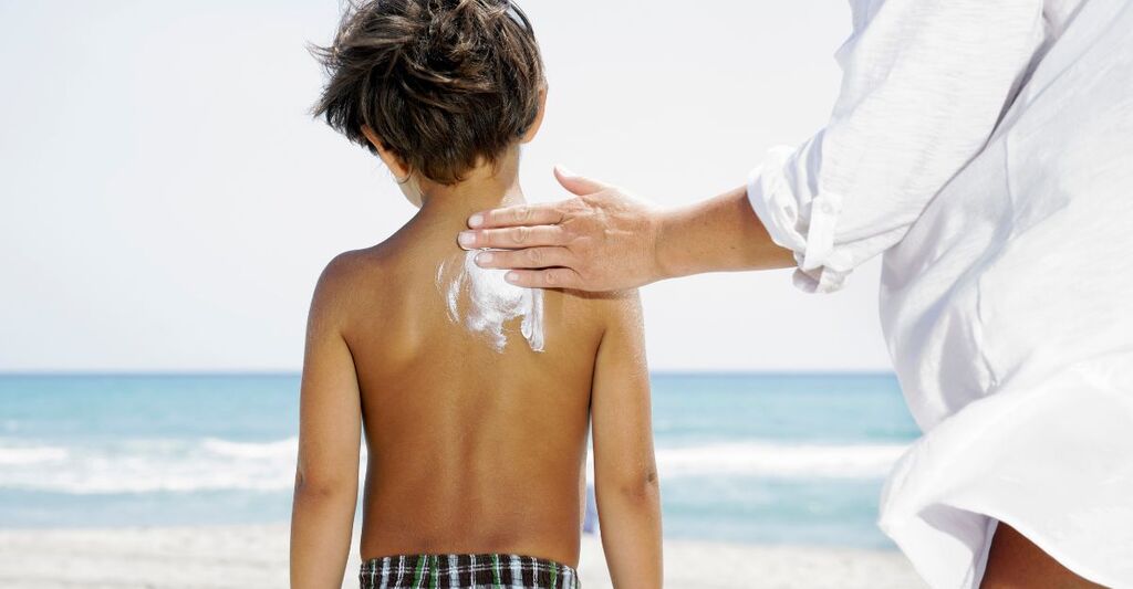 Un genitore che mette la crema solare al figlio in spiaggia