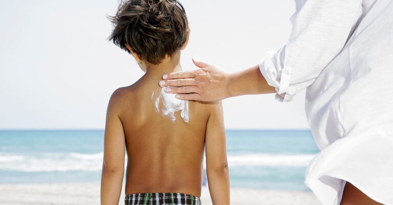 Un genitore che mette la crema solare al figlio in spiaggia