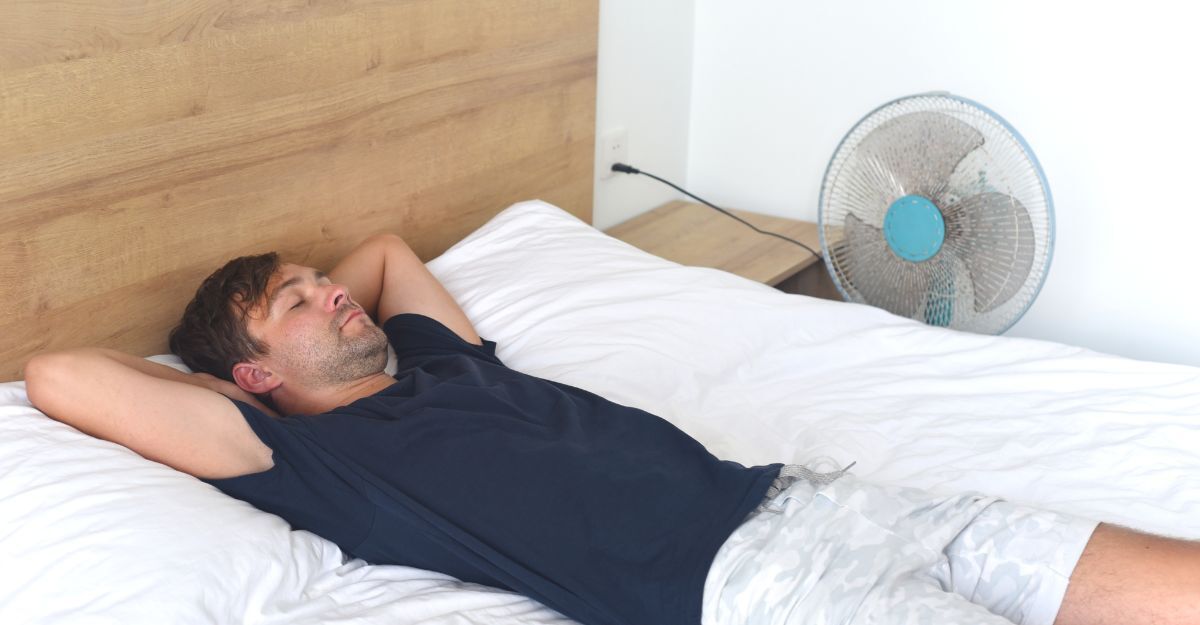 Un uomo che dorme sul letto con il ventilatore acceso