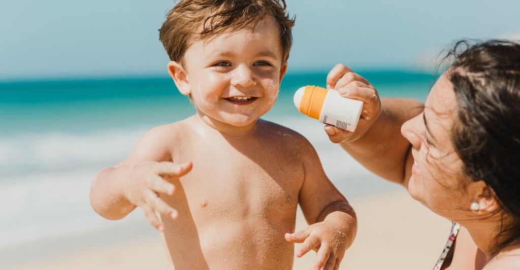 Una madre che mette la crema solare al figlio in spiaggia