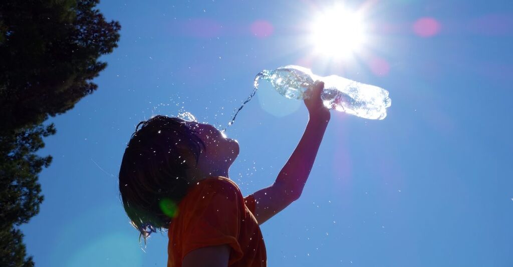 Un bambino beve acqua sotto il sole