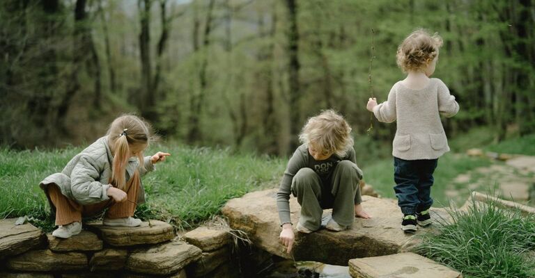 3 bambini giocano nel bosco, vicino ad un ruscello
