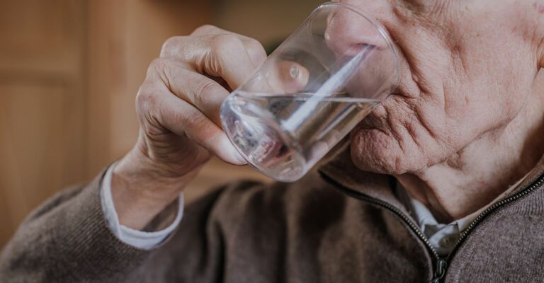 anziano beve un bicchiere d'acqua