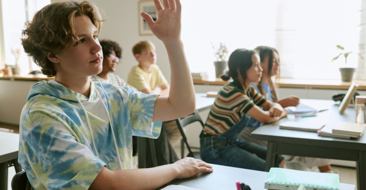 Un ragazzo con la mano alzata all'interno di una classe scolastica