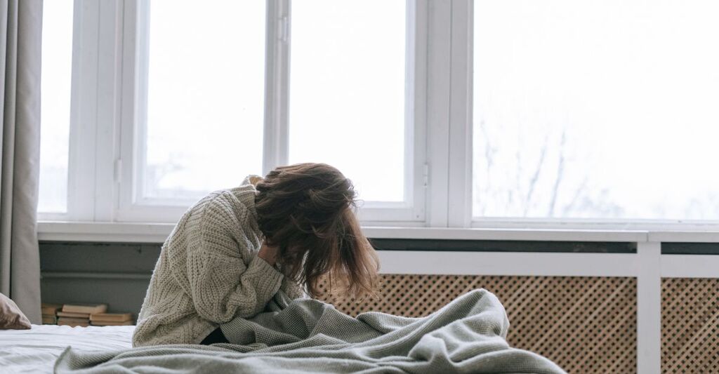 Una ragazza appena sveglia con le mani in faccia, disperata e stanca