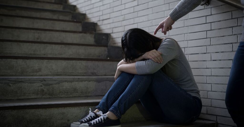 Una ragazza seduta sulle scale con la testa tra le gambe indicata da un bullo