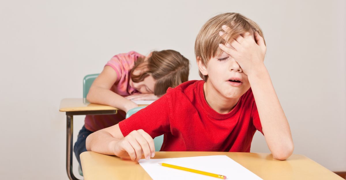 bambino seduto sul banco, si tocca la faccia stanco