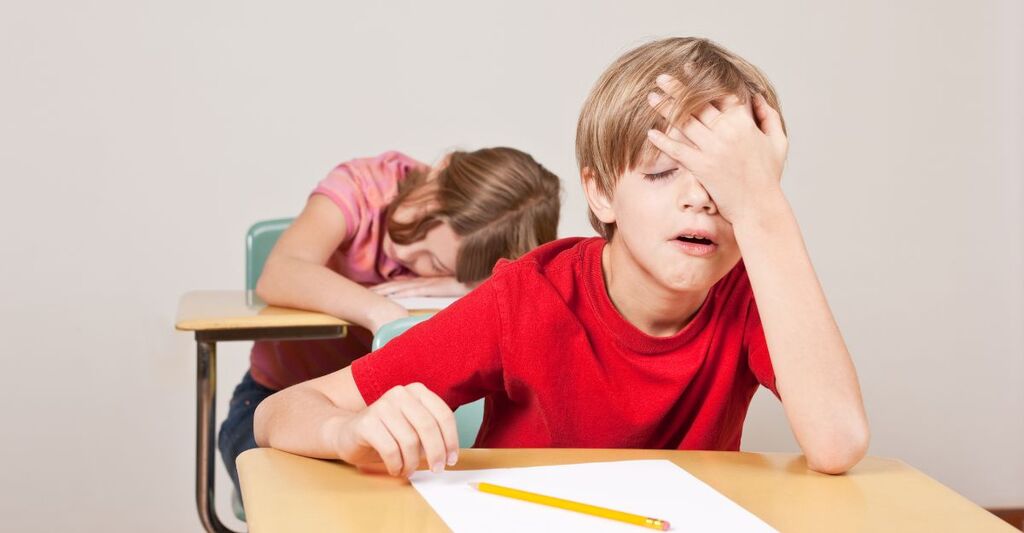 bambino seduto sul banco, si tocca la faccia stanco