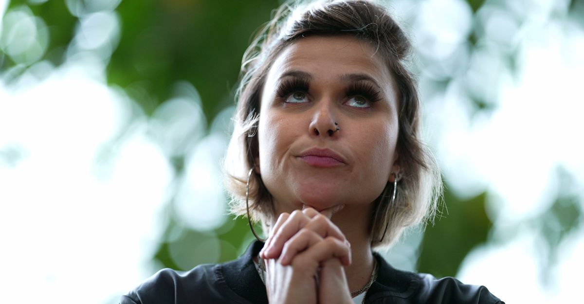 Primo piano di una donna con le mani giunte sotto il mento che guarda verso l'alto pensierosa
