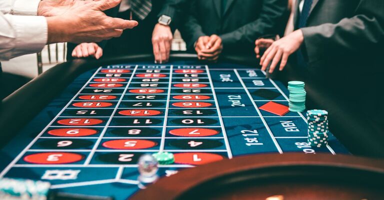 Mani di giocatori attorno a un tavolo da roulette in un casinò, con fiches puntate sui numeri.   