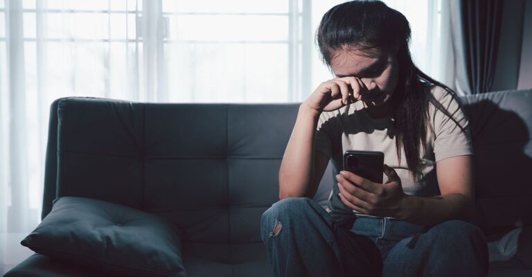 ragazza triste guarda il cellulare sul divano