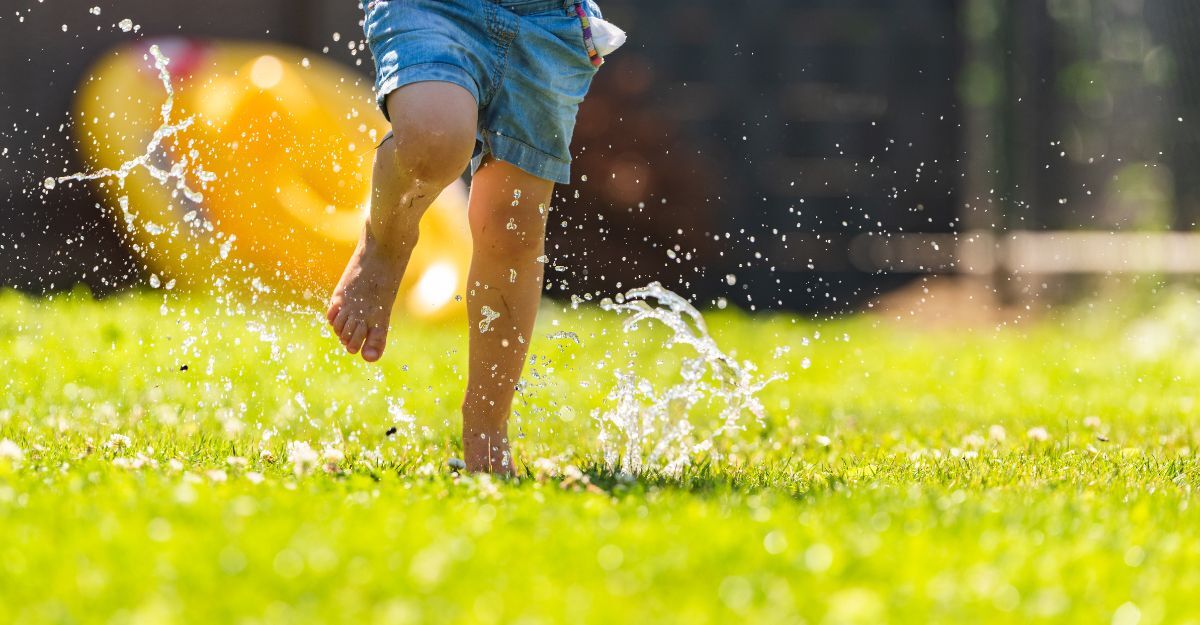 Bambino a piedi nudi che corre su un prato verde giocando con gli schizzi d'acqua