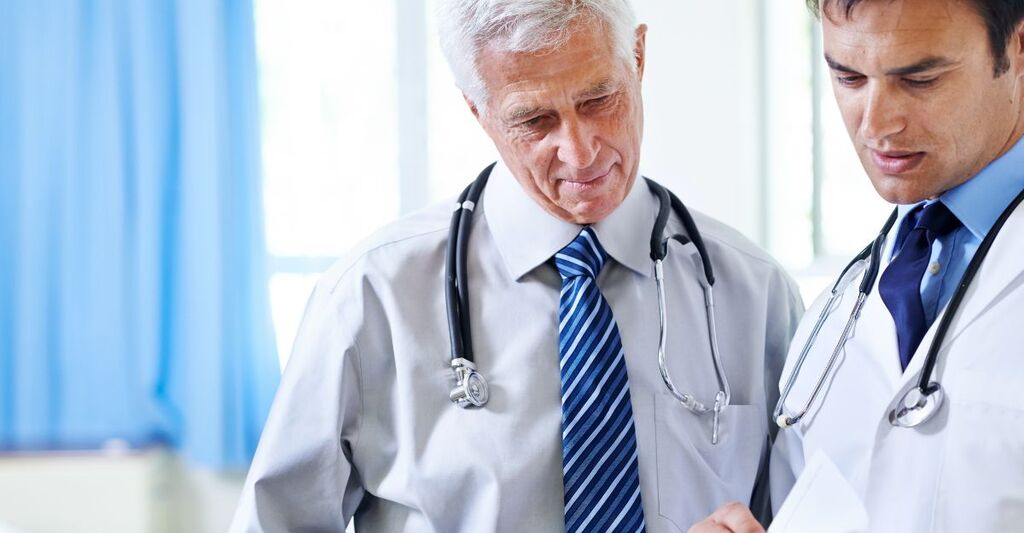 Due medici, un professionista più anziano e uno più giovane, intenti a consultare insieme dei documenti clinici in un ambiente ospedaliero o di studio medico