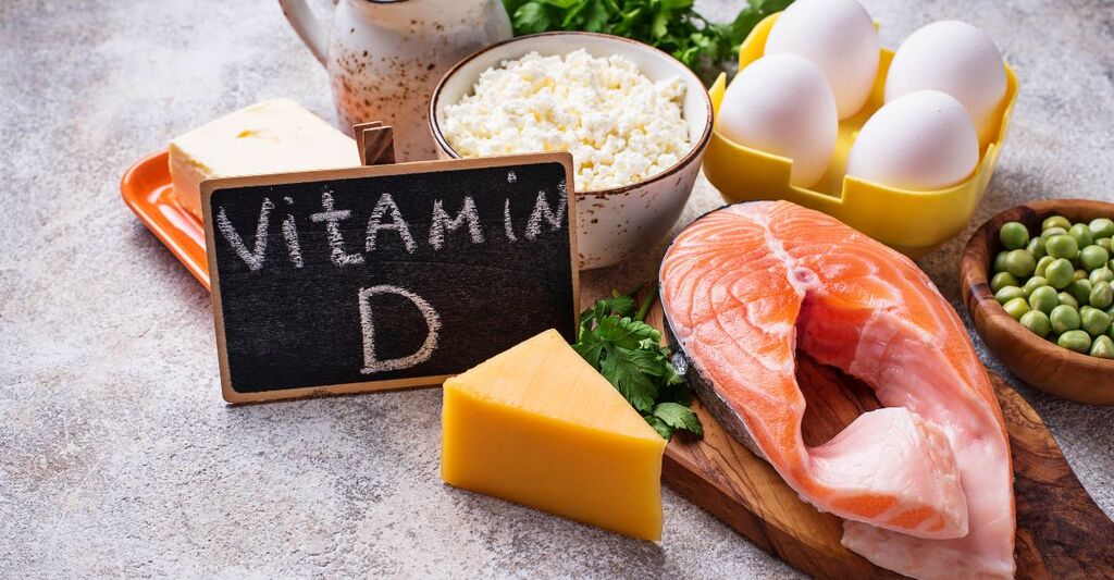 Varietà di cibi ricchi di vitamina D, tra cui un filetto di salmone fresco, uova, formaggio e una lavagnetta con la scritta "Vitamin D"