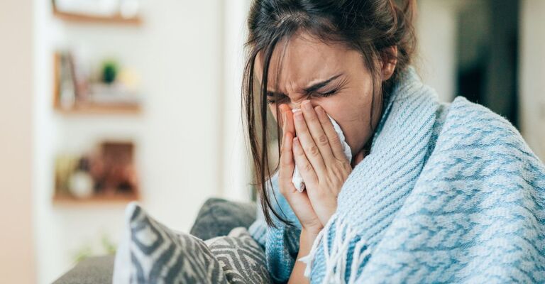 Primo piano di una donna con una coperta azzurra sulle spalle mentre si soffia il naso intensamente