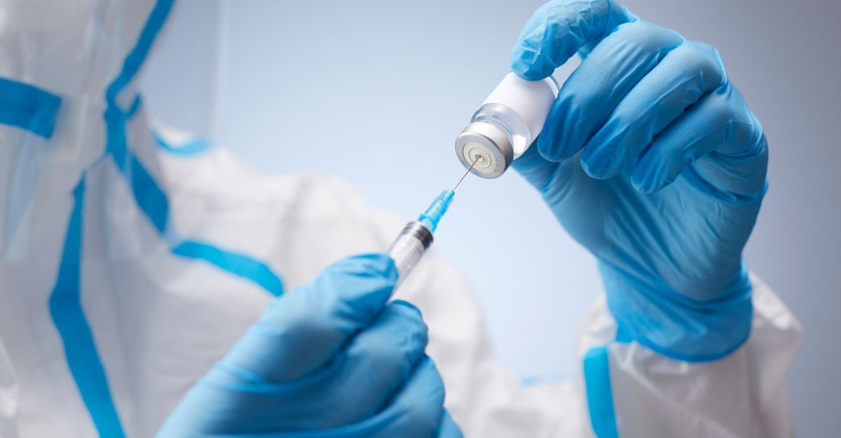Operatore sanitario con guanti blu e tuta protettiva che preleva il siero da una fiala con una siringa