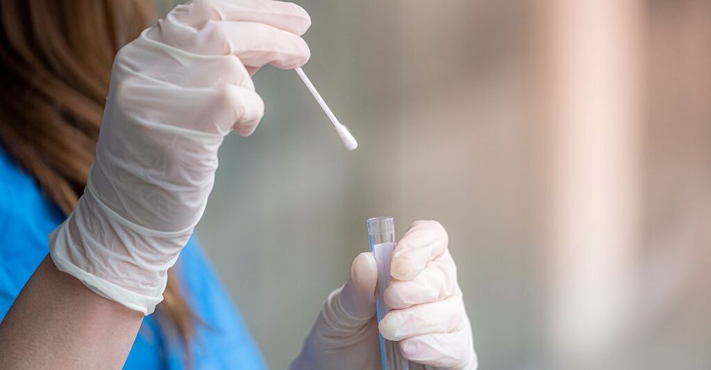 Operatore sanitario con guanti bianchi mentre inserisce un tampone nasofaringeo in una provetta da laboratorio