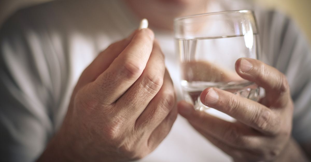 Una signora anziana che prende una pastiglia con dell'acqua