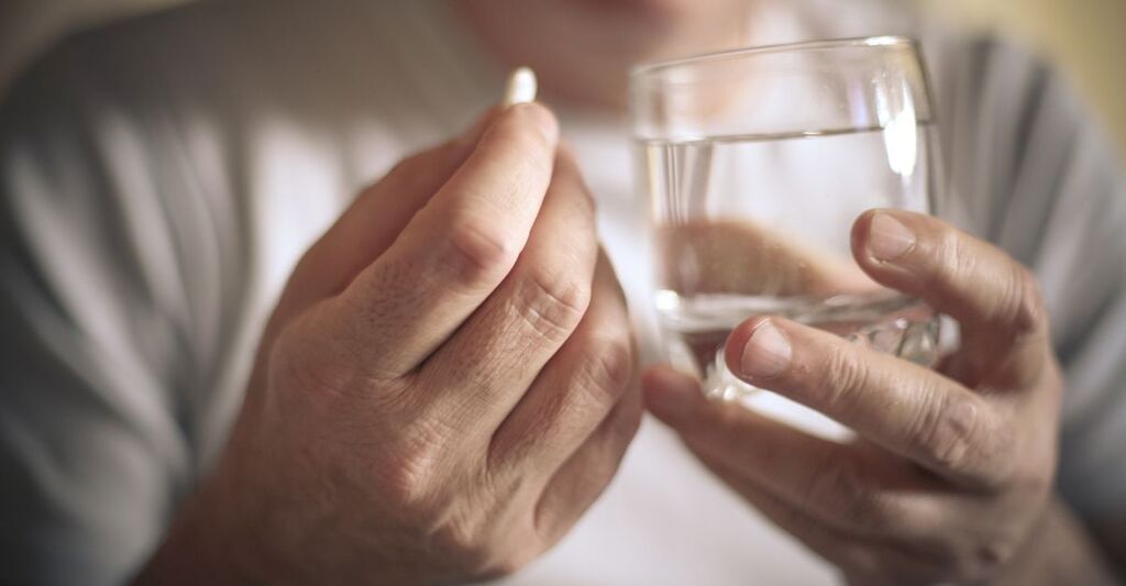 Una signora anziana che prende una pastiglia con dell'acqua