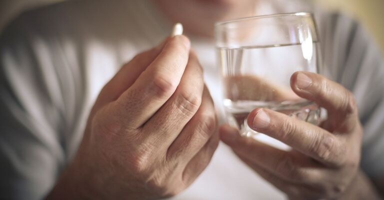 Una signora anziana che prende una pastiglia con dell'acqua