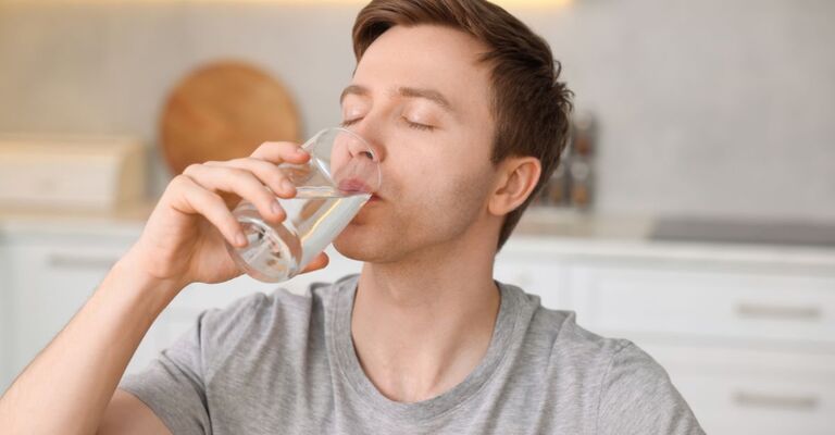 Un ragazzo che beve un bicchiere d'acqua fresca all'interno di una cucina