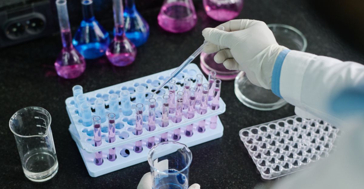 Mano con guanto sanitario che utilizza una pipetta graduata per trasferire campioni liquidi in una serie di provette da laboratorio