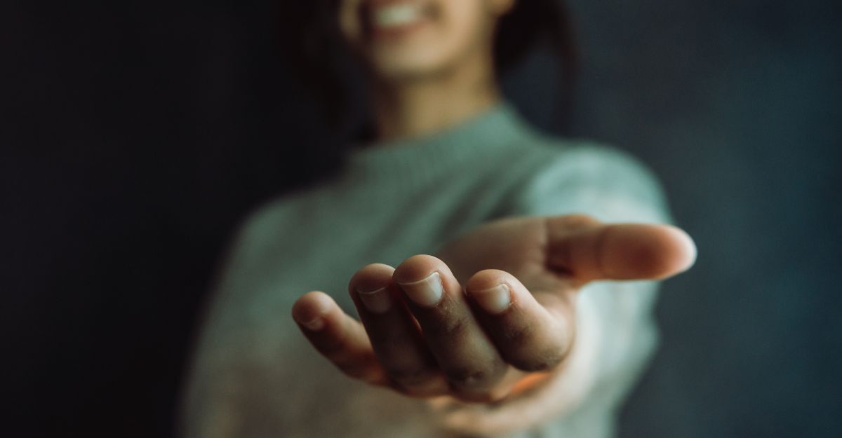 Primo piano di una mano tesa in avanti verso l'osservatore in un gesto di aiuto o supporto, con una figura sfocata sullo sfondo