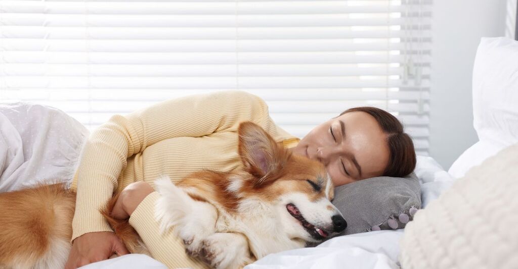 Una donna coricata a letto mentre dorme serenamente abbracciando il suo cane Corgi