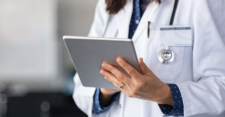 Un medico in camice bianco con uno stetoscopio al collo mentre consulta dei dati su un tablet digitale