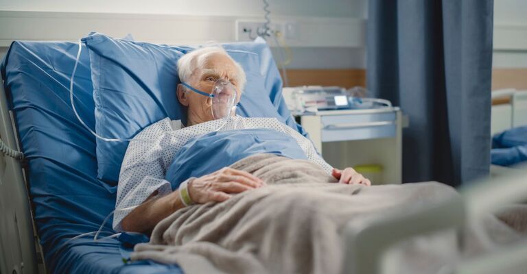 Anziano degente allettato in un letto d'ospedale con una maschera per l'ossigeno sul viso