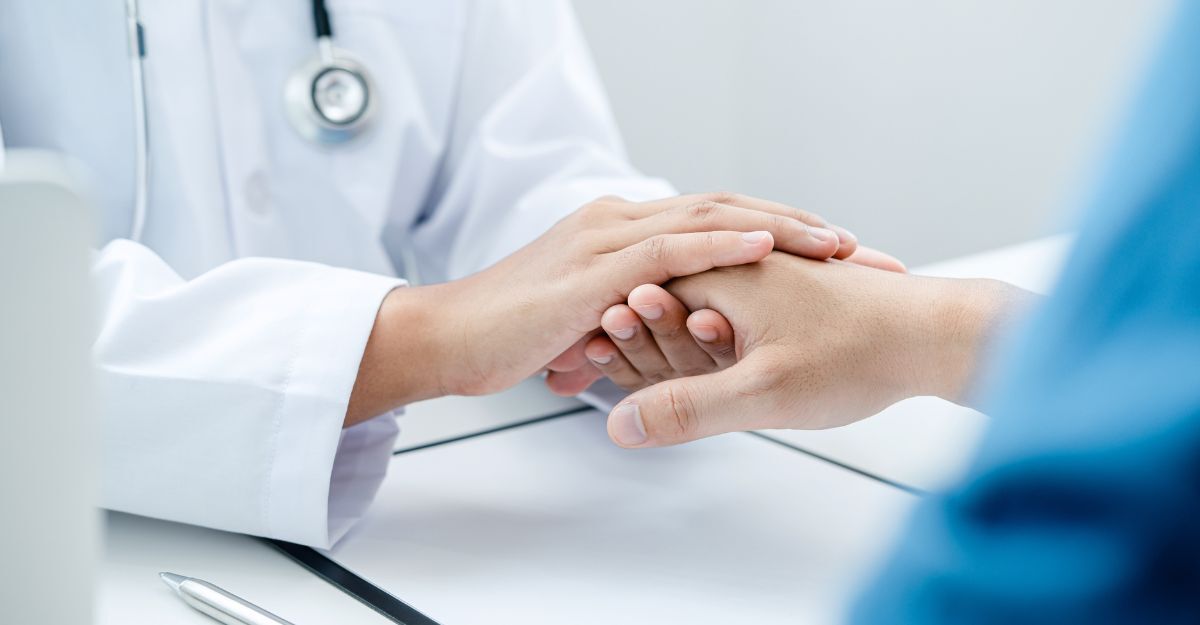 Primo piano delle mani di un medico in camice bianco che stringono e confortano con empatia la mano di un paziente durante un consulto