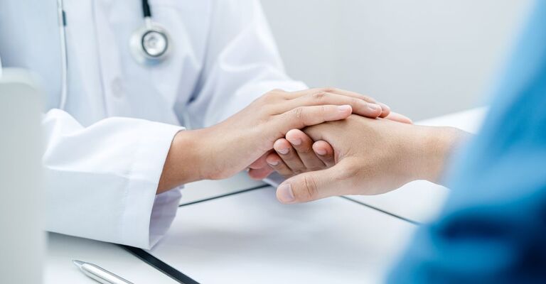 Primo piano delle mani di un medico in camice bianco che stringono e confortano con empatia la mano di un paziente durante un consulto