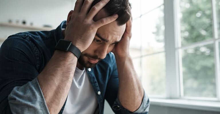 Un uomo con le mani alla testa e lo sguardo rivolto verso il basso in un momento di forte ansia o stress