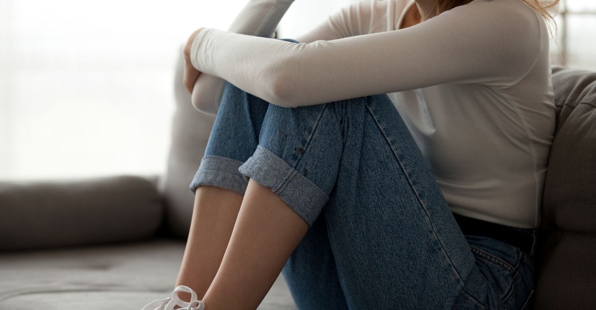 Una persona seduta su un divano rannicchiata con le ginocchia al petto e le braccia intorno alle gambe