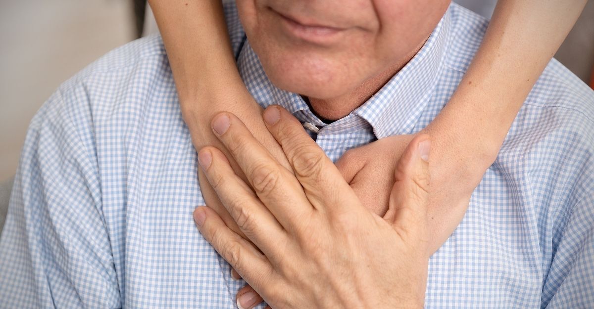 Primo piano delle mani di una persona giovane che abbracciano da dietro le spalle di un uomo anziano in camicia a quadri, che ricambia stringendole con affetto