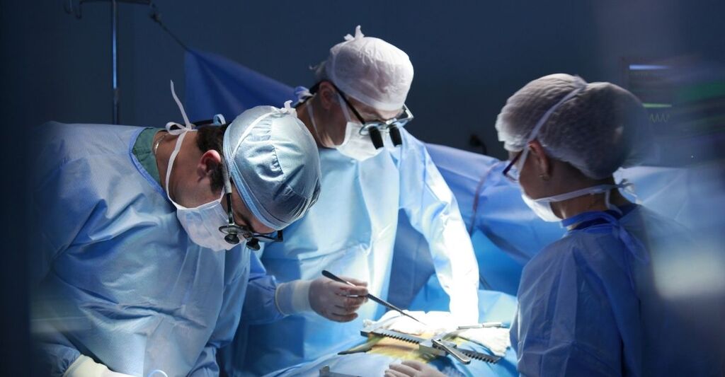 Equipe di chirurghi con camici stereo, mascherine e occhiali ingranditori concentrata durante un intervento chirurgico in sala operatoria