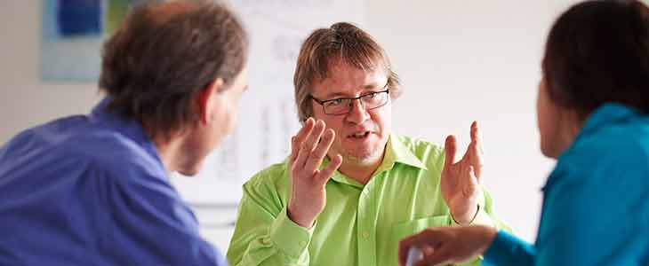 730x300 Mann mit gr&uuml;nen Hemd spricht mit 2 Personen