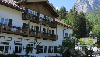 Aussenansicht des Hotels Berghotel Hammersbach ist zu sehen. Im Hintergrund gibt es Bäume und Berge