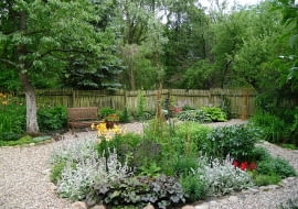 W wilgotnym, lekko zacienionym miejscu rosną funkie, tawułki i języczki. Z ceramicznej beczki pod nieczynną pompą 'wypływają' smagliczki