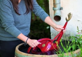 OFrau schpft Wasser aus WasserfassGiekanne : Garpa Tel. 0 41 52 / 92 52 00