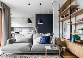 Salon otwarty na kuchnię. Aranżacja w kolorach granatu, szarości, bieli, z dodatkiem drewna