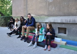 Przyzba "Architekci prekursorskich modernistycznych osiedli społecznych mieli świadomość, że większość przyszłych mieszkańców to pierwsza miejska generacja, która wprowadzi się do miasta wraz ze swoimi potrzebami i przyzwyczajeniami. Myśląc o nowej wspólnocie ułatwiali miejską adaptację, tworząc przestrzeń społeczną z przydomowymi elementami małomiasteczkowych ulic i wiejskiej zabudowy. Podwórze wymiarowali krokiem malucha idącego do przedszkola i wzrokiem staruszka wysiadującego na przyzbie. Na osiedlowym dziedzińcu ważne było przedproże przytrzymujące sąsiadów na krótką pogawędkę, bramki do rozwieszania prania, urządzenia dziecięce, lustro przy wyjściu dla zabieganych w obejściu, okienko z sieni dla wypatrujących listonosza, wysoki próg przy kurzącej się ulicy, balustrady z miejscem na skrzynki kwiatowe i kosze na odstawianie zakupów przy furtce. Na skutek procesu industrializacji, po dekadach standaryzacji, unifikacji i banalizacji atrybuty przestrzeni społecznej zanikły, zostały same bloki. Przywracamy przyzbę do przestrzeni społecznej."